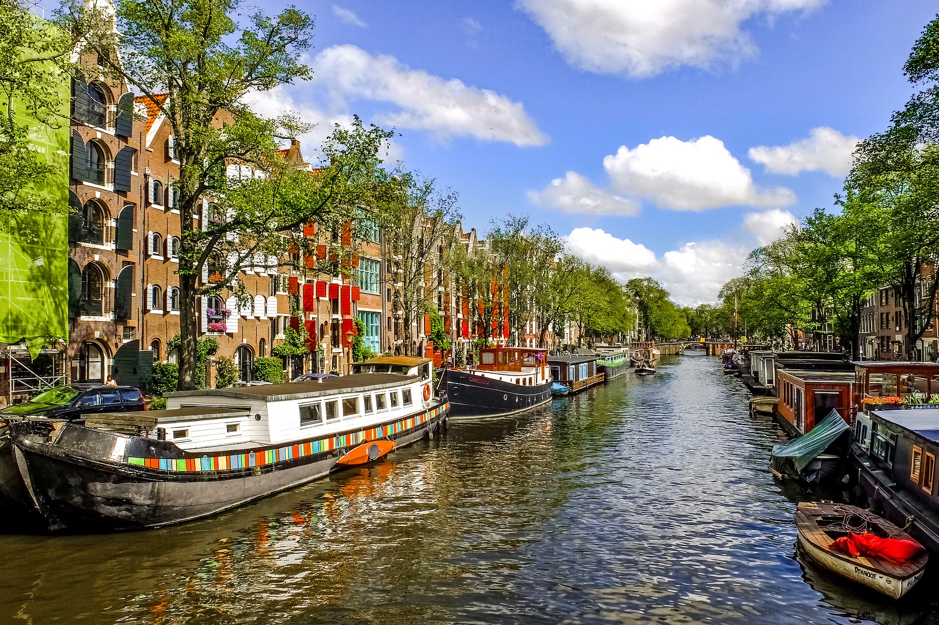 Busreise Amsterdam Grachtenfahrt Kanal kleine Schiffe bunte Häuser grüne Bäume